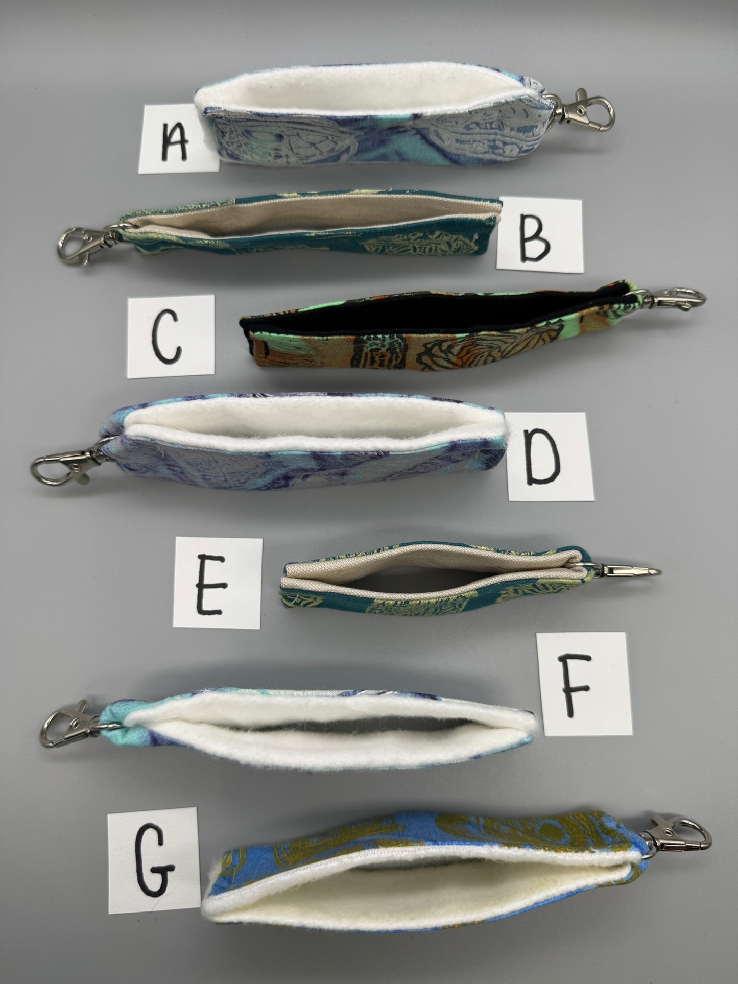 Set of fabric pouches with keychains labeled A to G on a gray background